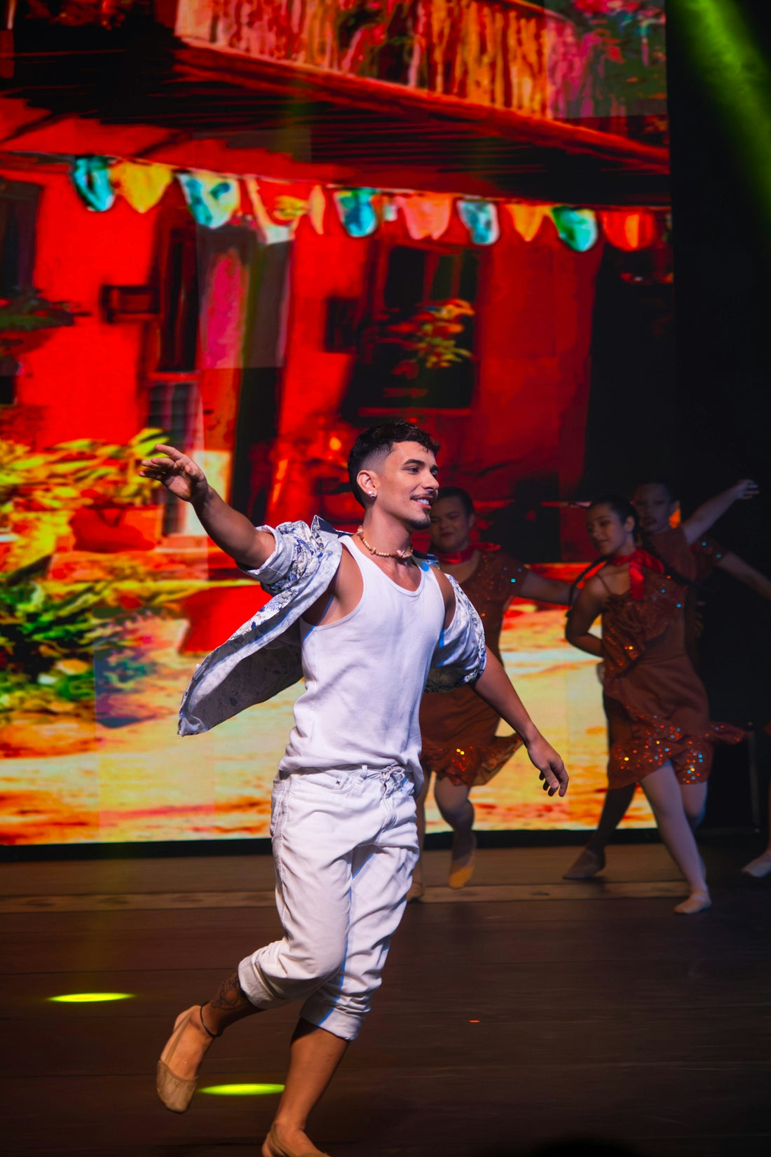 Smiling male dancer in white performing against a vibrant backdrop.